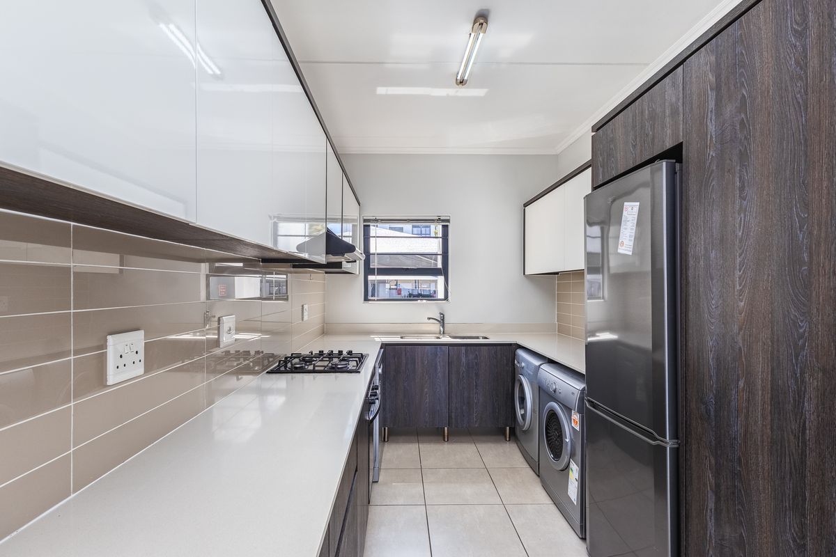 Modern galley-style kitchen featuring high-gloss cabinetry, stone countertops, gas hob, extractor fan, and integrated laundry appliance connections.