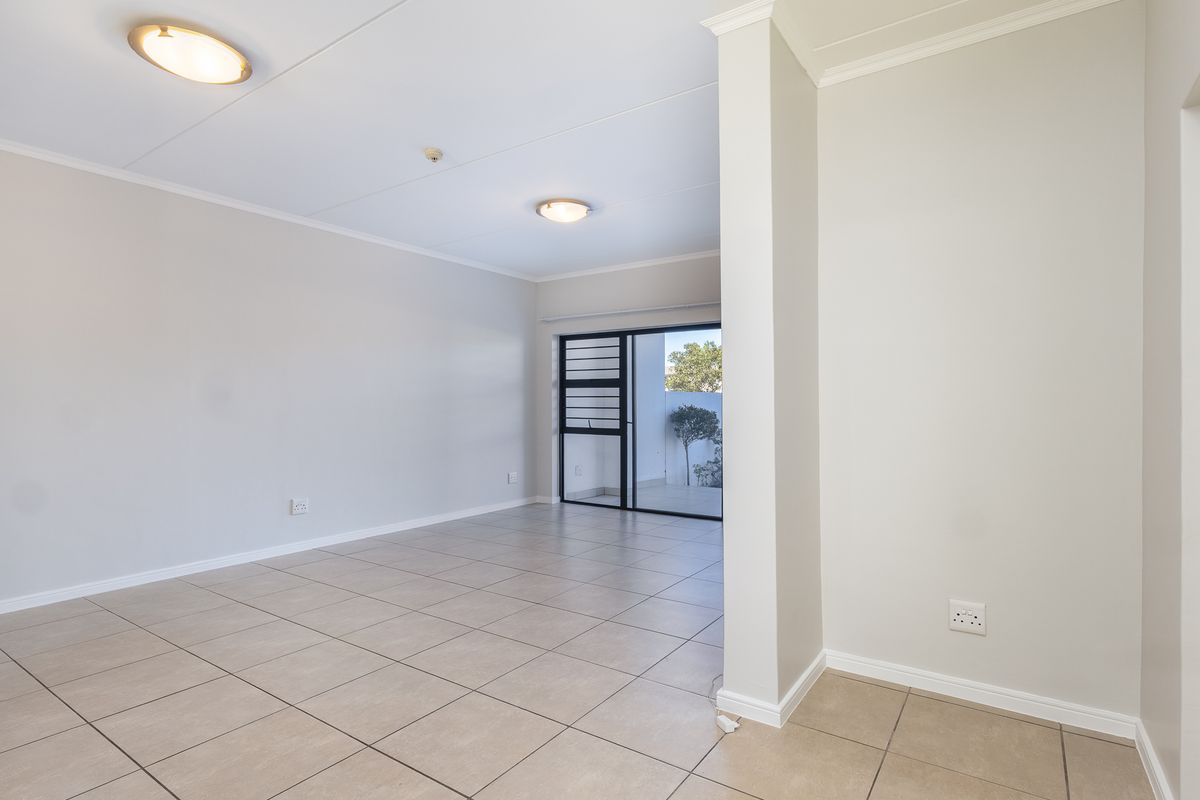 A bright, empty living area featuring neutral tiled flooring, clean walls, and a sliding glass door providing access to an outdoor space.
