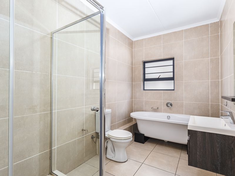 A modern, well-maintained bathroom featuring a freestanding bathtub, a separate glass-enclosed shower, a vanity basin, and neutral floor-to-ceiling wall tiles.