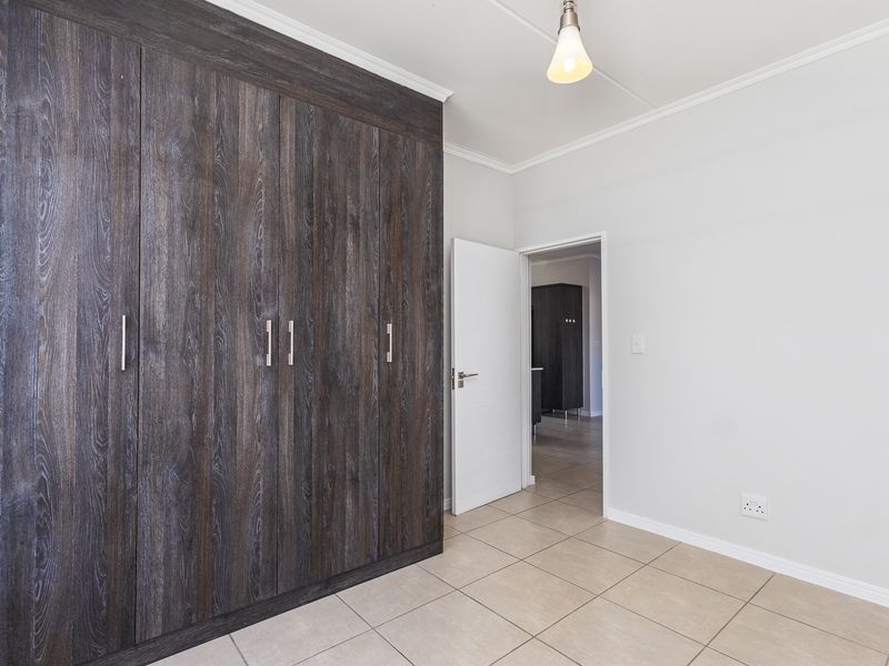 A clean, empty bedroom featuring dark wood-grain built-in cupboards, neutral tiled flooring, and a simple pendant light fixture.