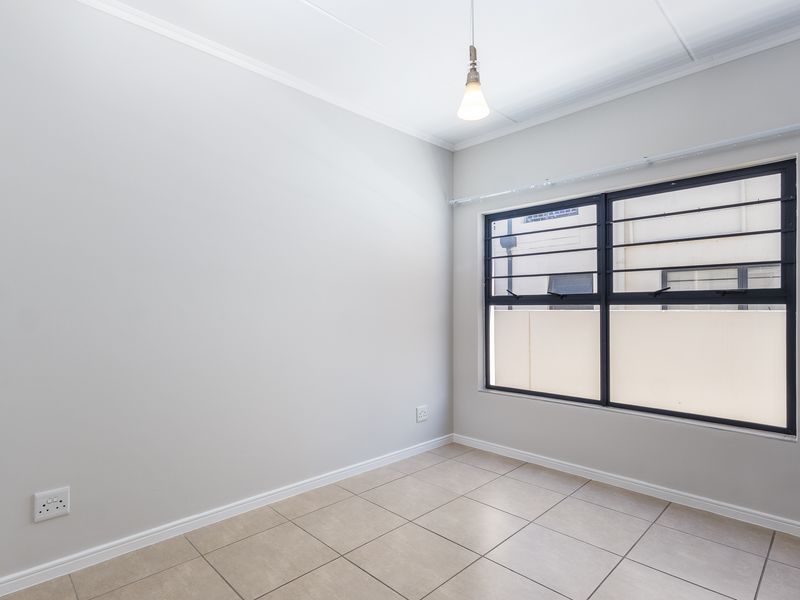 A clean, empty bedroom featuring neutral tiled flooring, a large window with security bars, and a simple pendant light fixture.