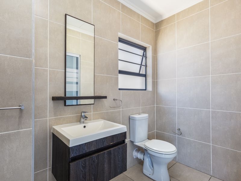 A clean, modern bathroom featuring neutral wall tiles, a floating vanity cabinet with a basin, and a louvered window for ventilation.