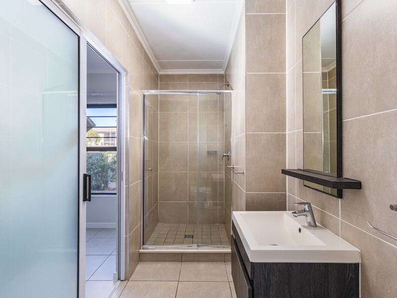 A modern, well-maintained bathroom featuring a glass-enclosed shower, vanity with basin, and neutral floor-to-ceiling tiling.