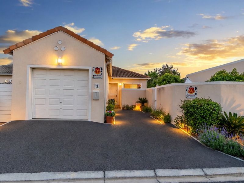 A well-maintained front elevation featuring a single garage, paved driveway, and perimeter boundary wall with integrated exterior lighting at dusk.