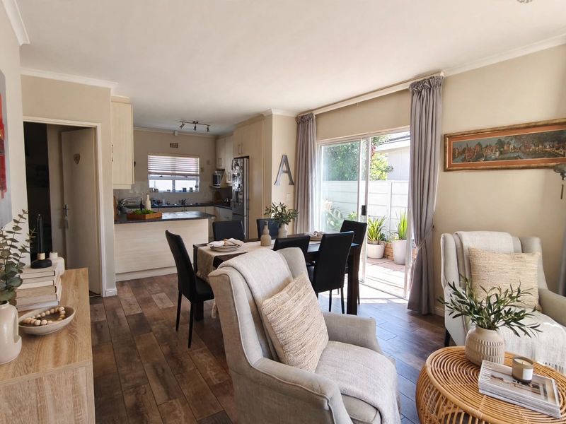 An open-plan living and dining area featuring laminate flooring, neutral walls, and a seamless transition to an outdoor patio through sliding glass doors.