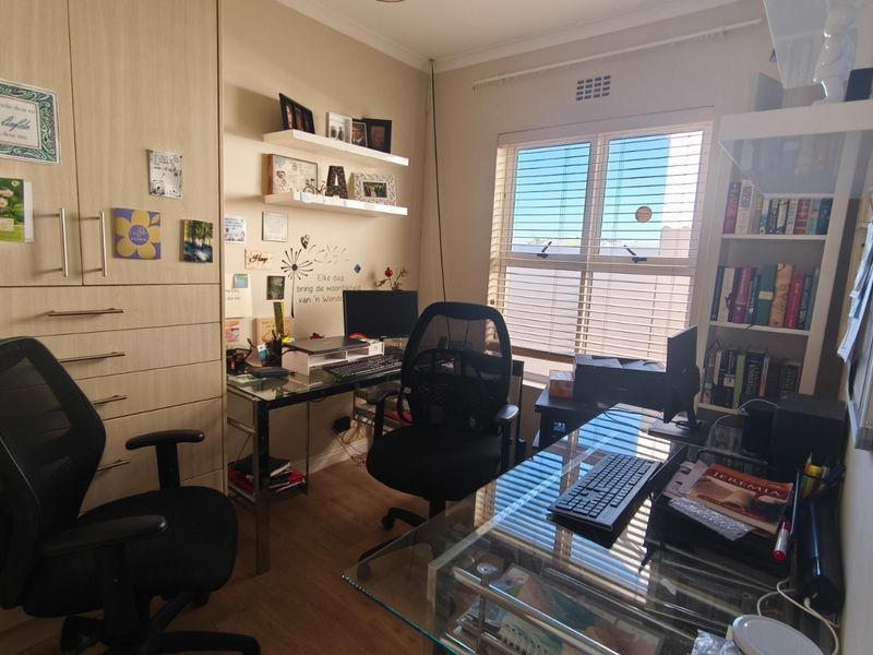 A functional home office featuring built-in cabinetry, integrated shelving, laminate flooring, and natural light through a window with fitted blinds.