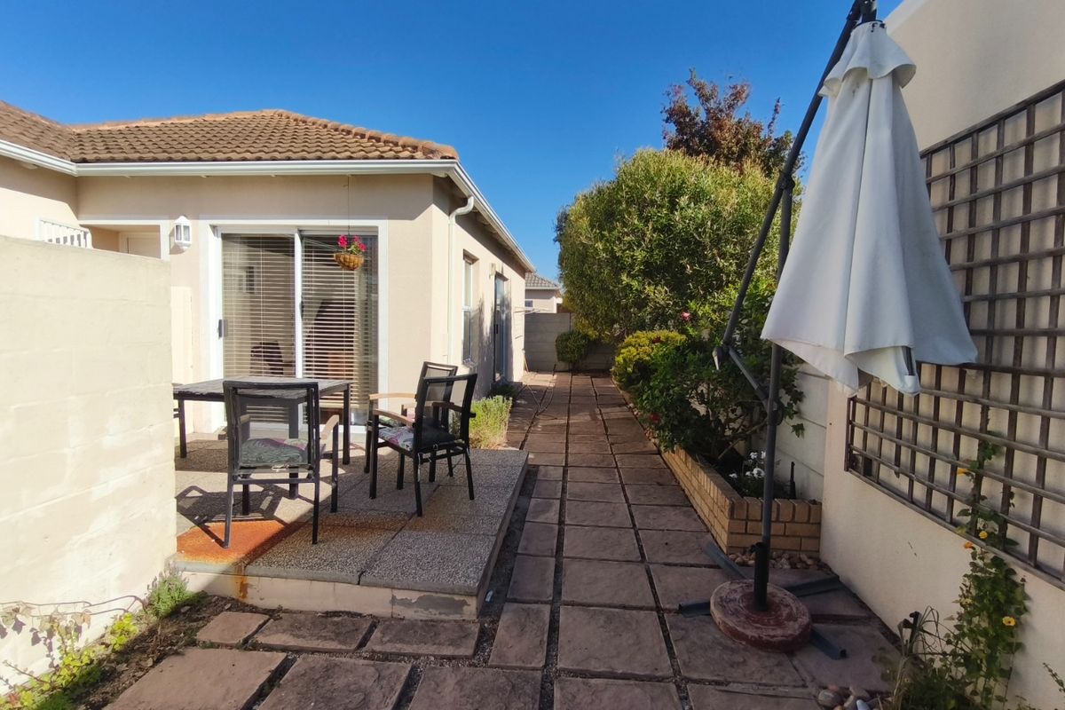 A rear exterior view featuring a paved patio area, sliding glass doors, and a garden path with established landscaping and a brick planter.