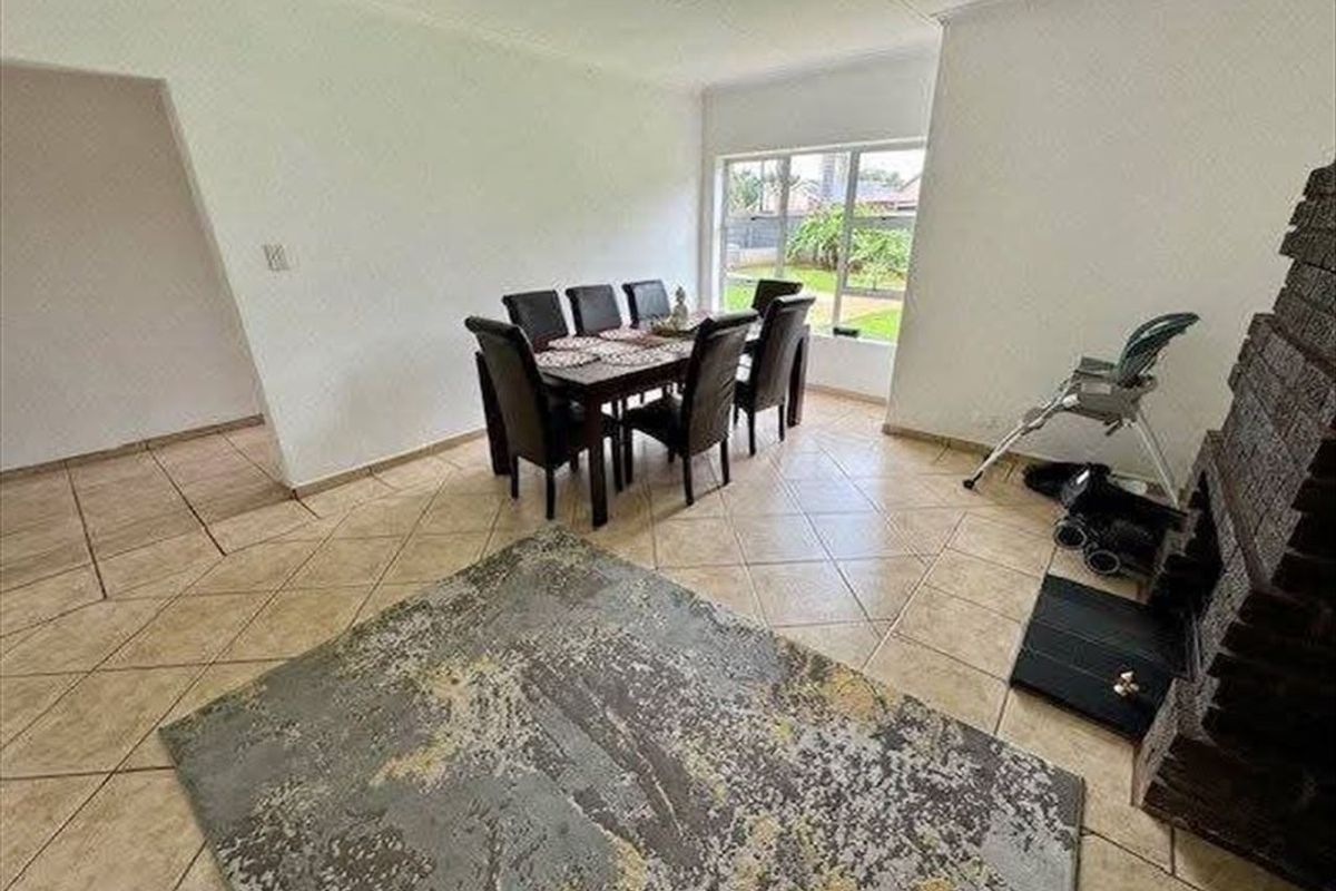 Spacious living area featuring tiled flooring, a prominent brick fireplace, and large windows providing natural light and garden views.