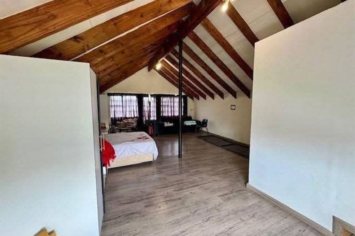 Spacious bedroom featuring a high vaulted ceiling with exposed timber rafters, laminate flooring, and a central support column.