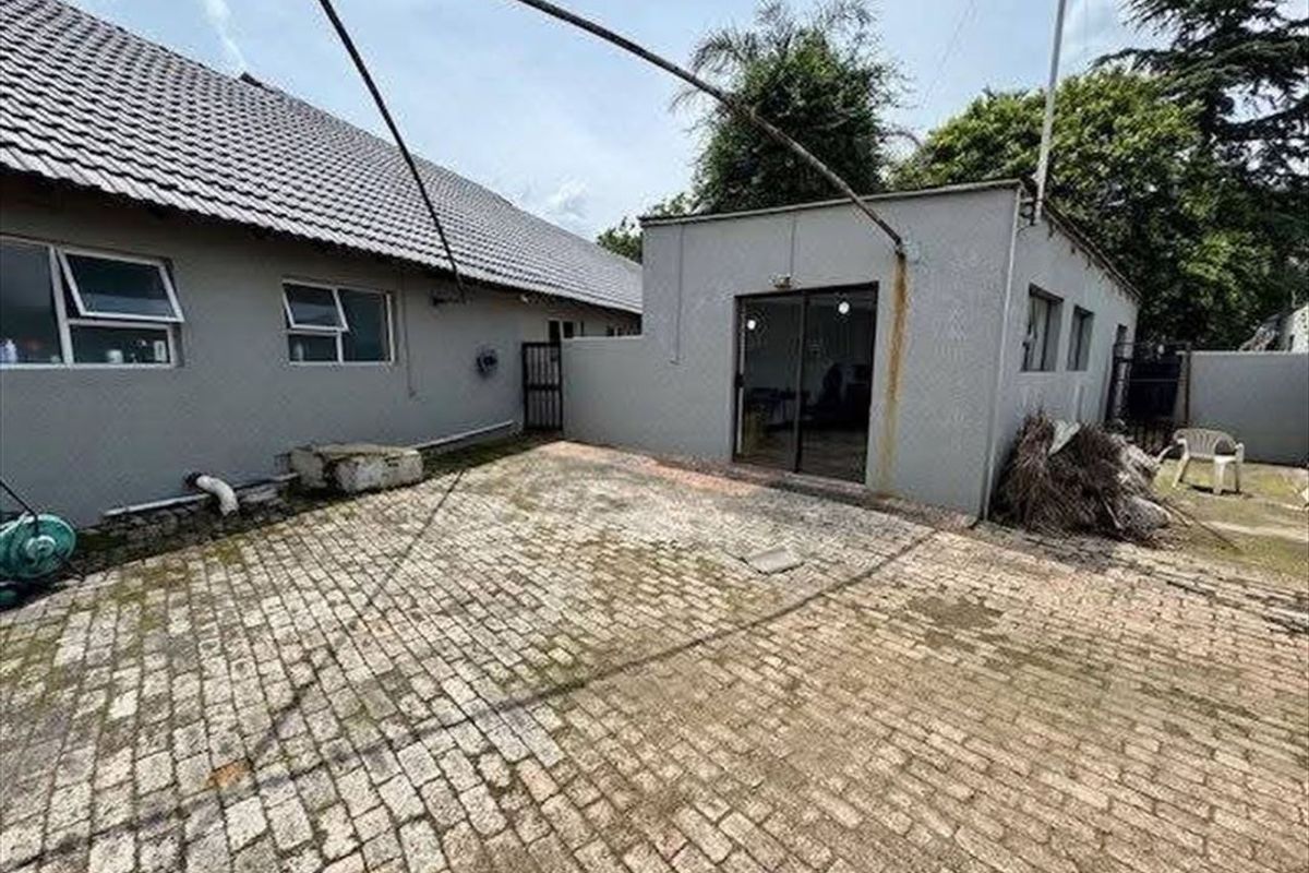 Rear exterior view of the property featuring a paved courtyard area, sliding door access, and tiled roof structure.