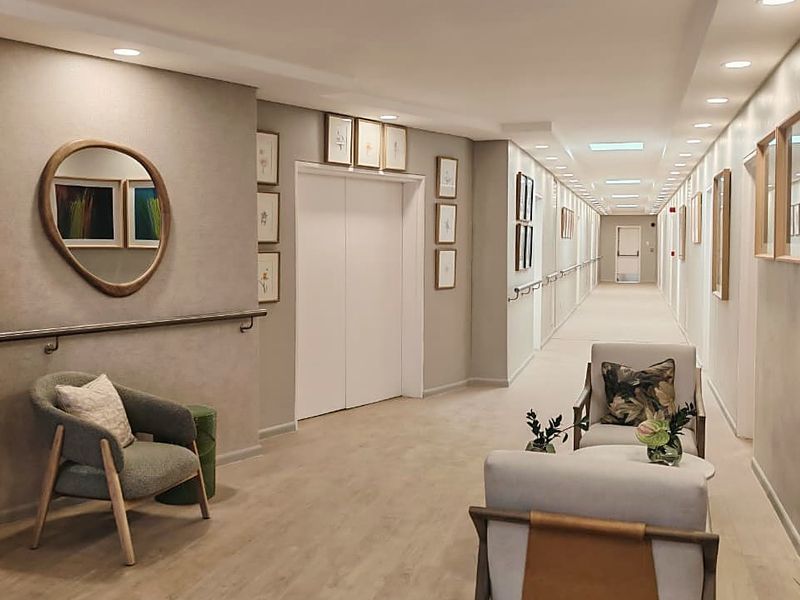 A well-maintained, modern apartment building hallway featuring recessed lighting, handrails, and elevator access with neutral finishes.