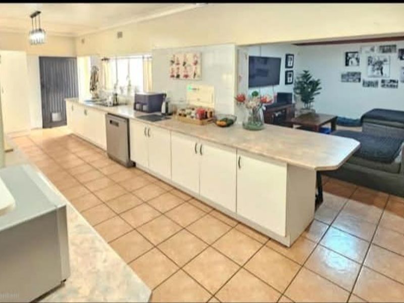 An open-plan kitchen and living area featuring tiled flooring, extensive built-in cabinetry, and laminate countertops, creating a functional and connected living space.