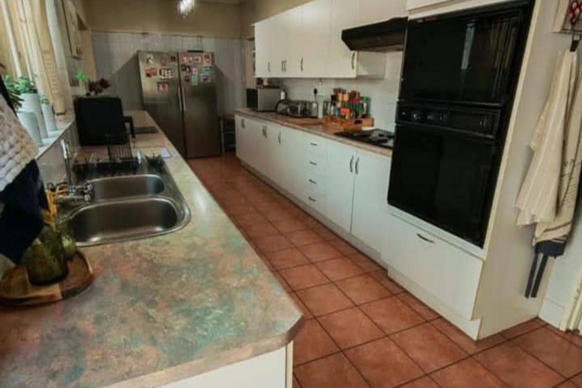 A functional galley-style kitchen featuring white cabinetry, built-in oven, extractor fan, double sink, and tiled flooring.