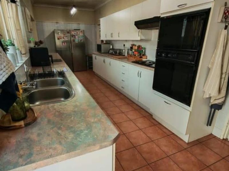 A functional galley-style kitchen featuring white cabinetry, built-in oven, extractor fan, double sink, and tiled flooring.