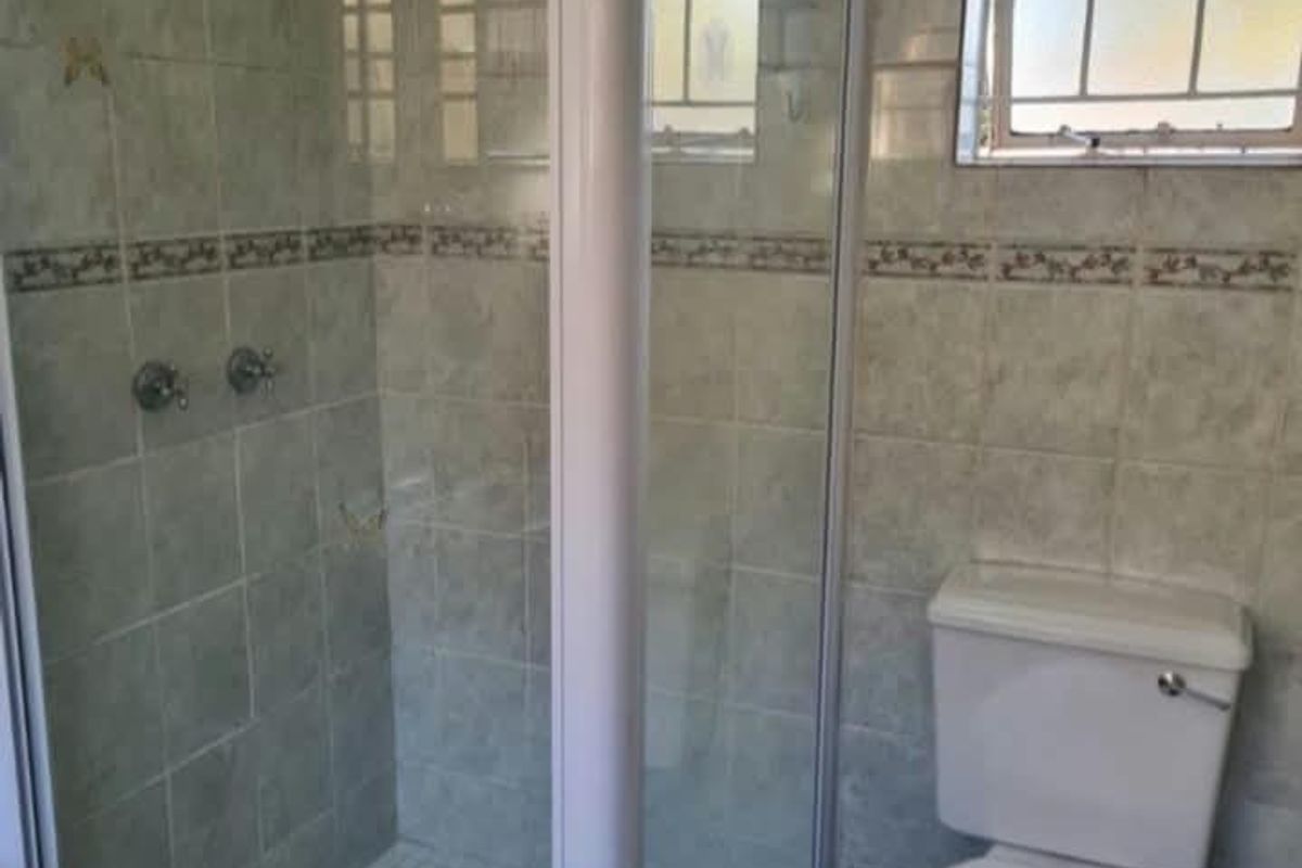 A functional bathroom featuring a glass-enclosed shower, a standard toilet, and neutral wall tiling with a decorative border.