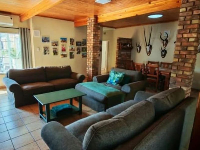 Spacious open-plan living and dining area featuring exposed timber ceilings, brick support columns, and tiled flooring throughout.