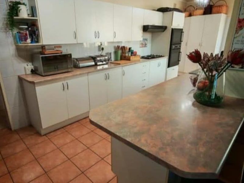 A functional kitchen featuring white cabinetry, laminate countertops, a kitchen island, and tiled flooring, providing a practical workspace for daily cooking and meal preparation.