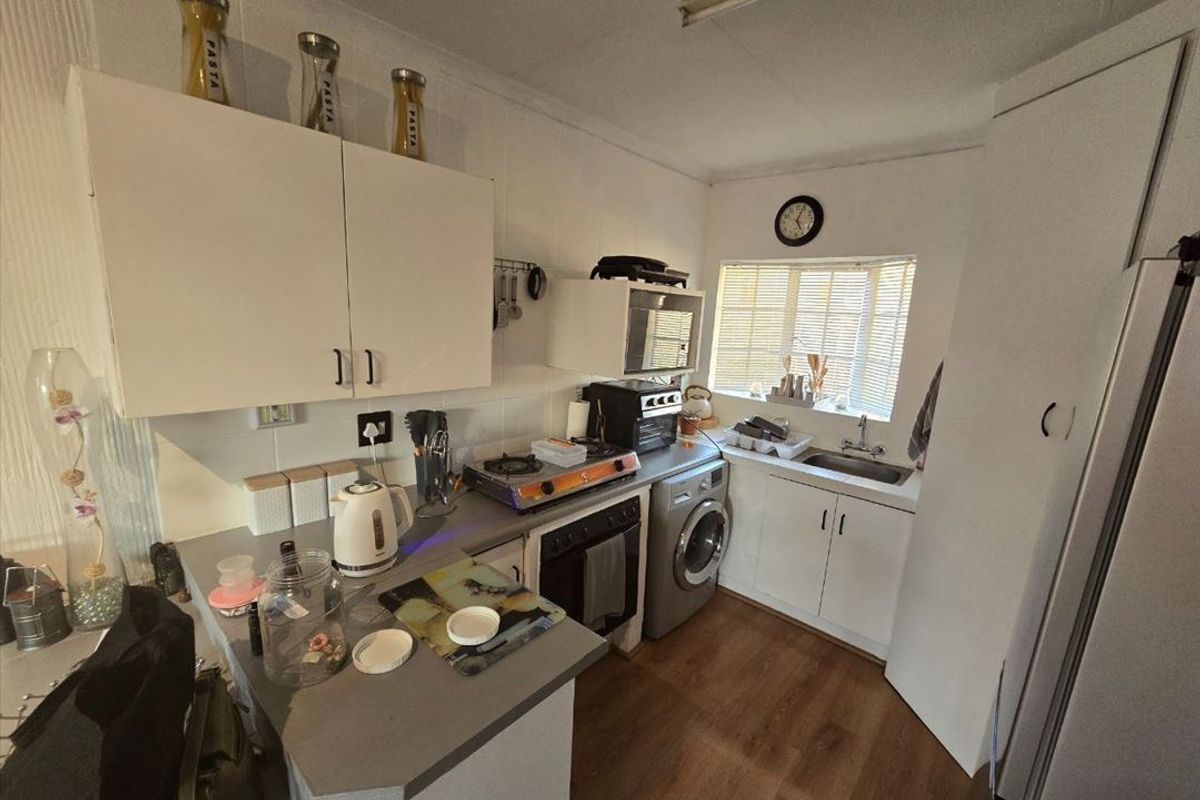 A compact kitchen featuring white cabinetry, laminate countertops, a built-in oven, and a stainless steel sink with natural light from a window.