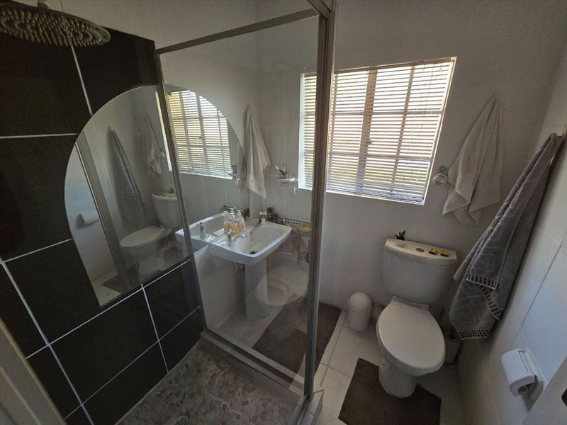 A functional bathroom featuring a pedestal washbasin, a toilet, and a glass-enclosed shower with a modern rain shower head and tiled finishes.
