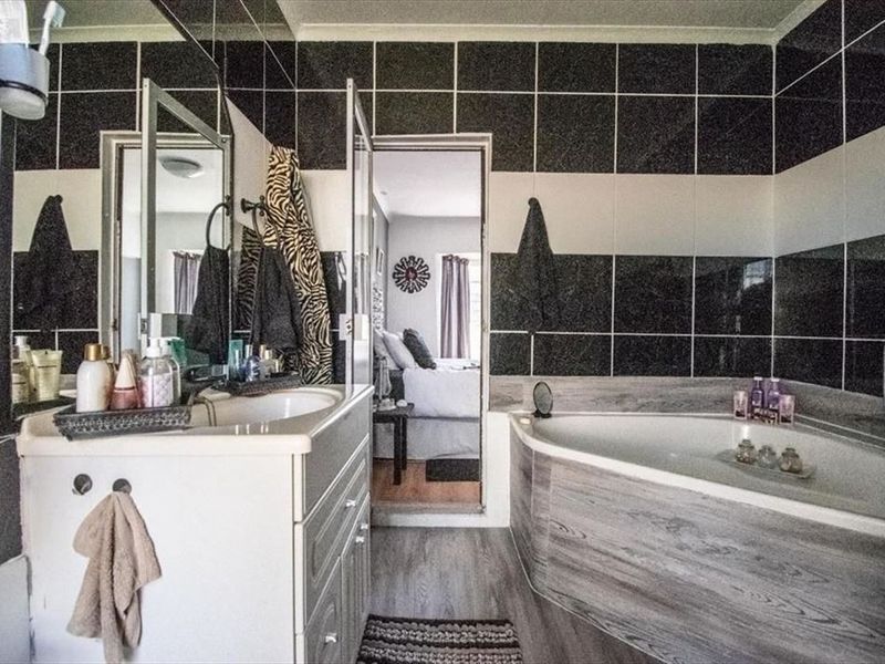 A bathroom featuring a corner bathtub, vanity cabinet with integrated sink, and contrasting black and white wall tiling.