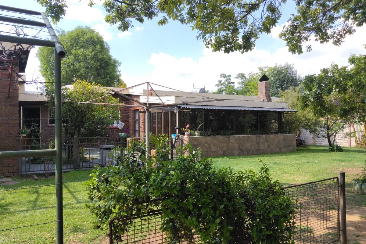 Rear view of the property featuring a covered patio area, brick chimney, and a spacious garden with established trees and perimeter fencing.