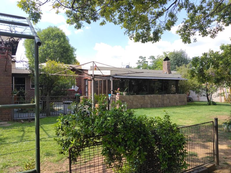 Rear view of the property featuring a covered patio area, brick chimney, and a spacious garden with established trees and perimeter fencing.