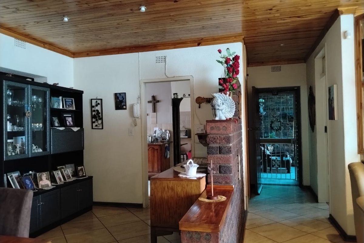 Living area featuring a timber tongue and groove ceiling, ceramic tiled flooring, and an exposed brick partition wall leading to the kitchen and entrance.