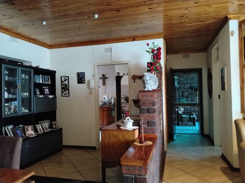 Living area featuring a timber tongue and groove ceiling, ceramic tiled flooring, and an exposed brick partition wall leading to the kitchen and entrance.