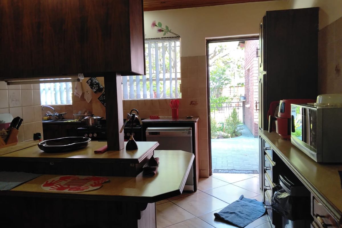 A functional kitchen featuring timber cabinetry, tiled surfaces, and direct access to an outdoor patio area.