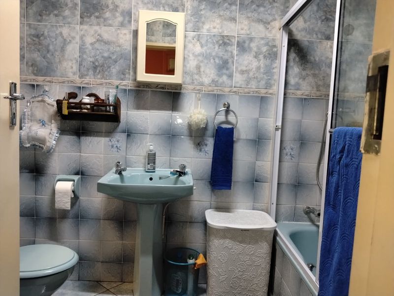 A dated bathroom featuring a pedestal basin, bathtub with shower screen, and blue-toned ceramic wall and floor tiles.