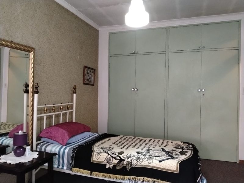 A bedroom featuring built-in cupboards with a light green finish and a textured accent wall.