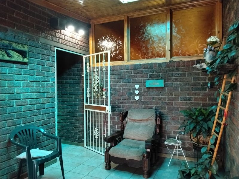A covered patio area featuring exposed brick walls, timber ceiling finishes, tiled flooring, and a secure metal gate entrance.