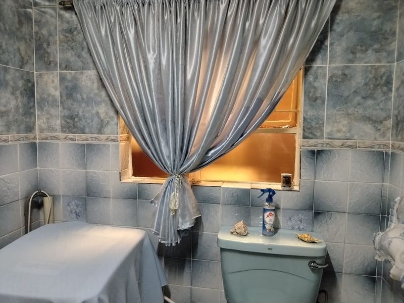 A bathroom featuring dated blue patterned ceramic wall tiles and a standard toilet cistern positioned beneath a window.