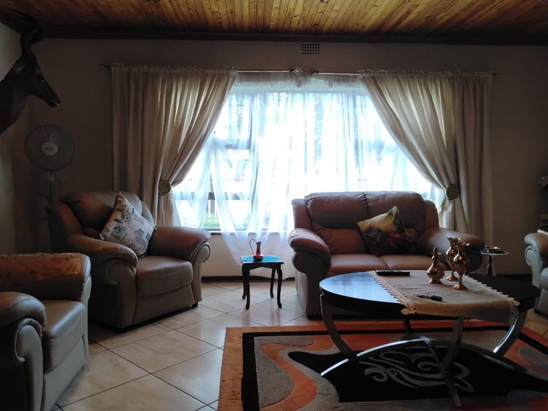 A cozy living room featuring a warm timber-paneled ceiling, neutral tiled flooring, and a large window that allows for natural light.
