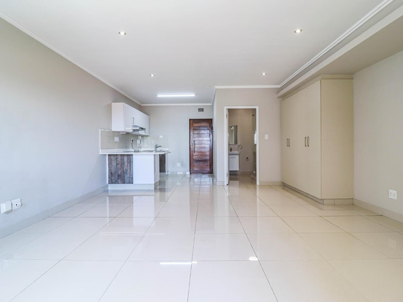 Spacious open-plan living area featuring tiled floors, built-in kitchen cabinetry, and ample storage cupboards, leading to a separate bathroom.