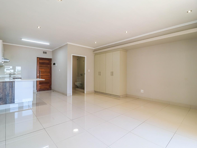 Spacious open-plan living area featuring modern tiled flooring, recessed lighting, a functional kitchen with built-in cabinetry, and ample storage cupboards.
