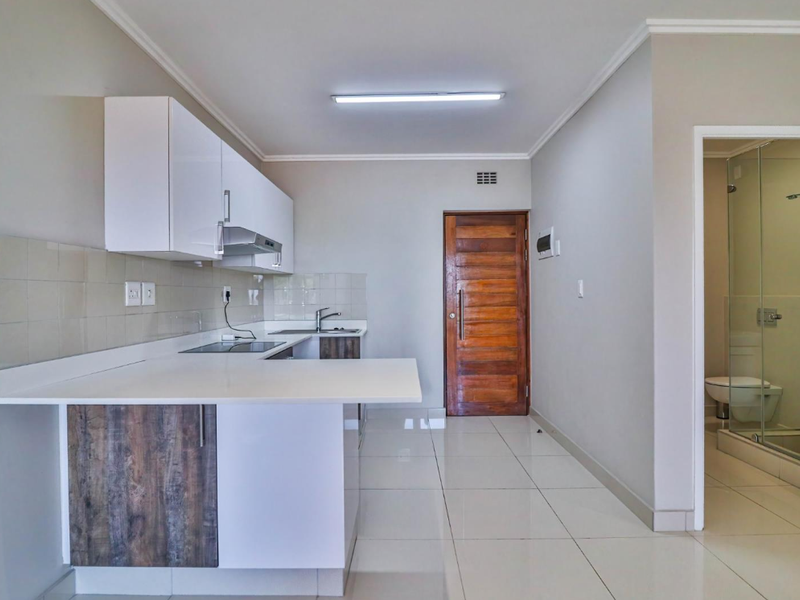 Open-plan kitchen featuring modern white cabinetry, stone countertops, and tiled flooring, with an adjacent bathroom visible through the doorway.