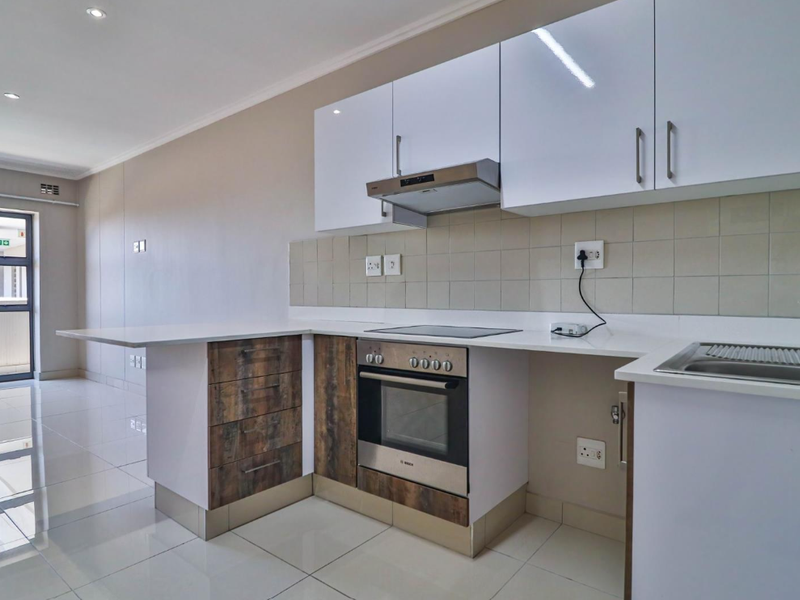 Modern kitchen featuring white gloss and wood-look cabinetry, integrated oven and hob, quartz countertops, and a tiled backsplash in an open-plan layout.