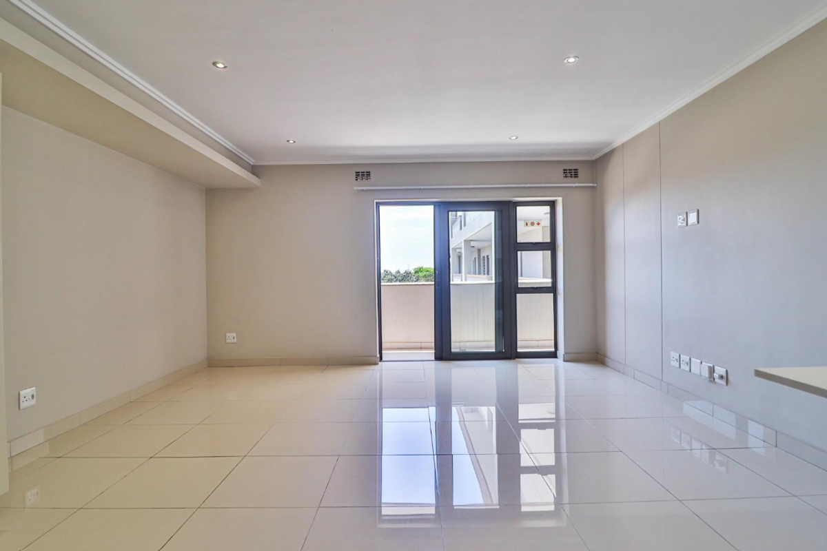 A bright, empty living room featuring neutral walls, polished tiled flooring, recessed lighting, and a sliding glass door leading to a balcony.