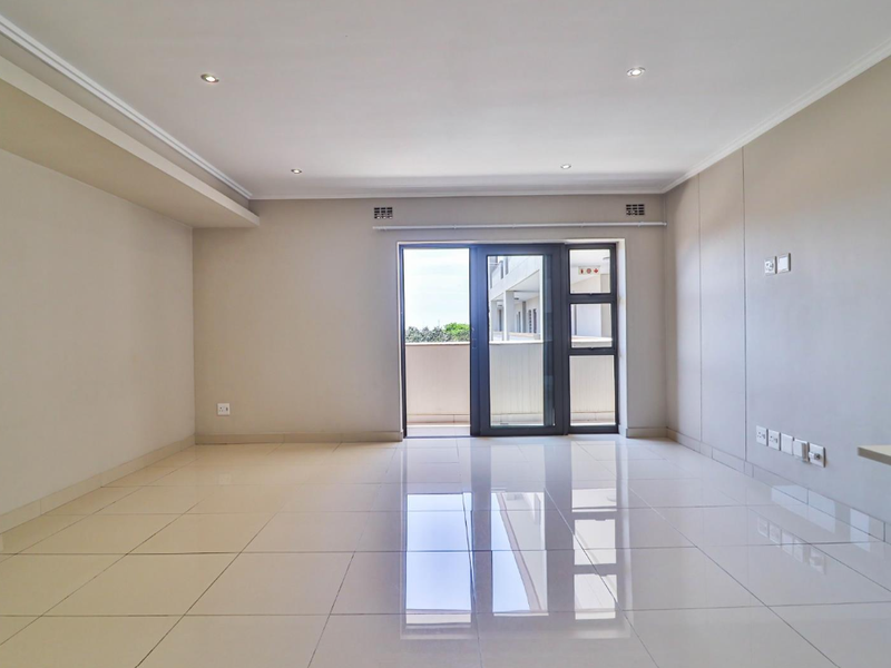 A bright, empty living room featuring neutral walls, polished tiled flooring, recessed lighting, and a sliding glass door leading to a balcony.