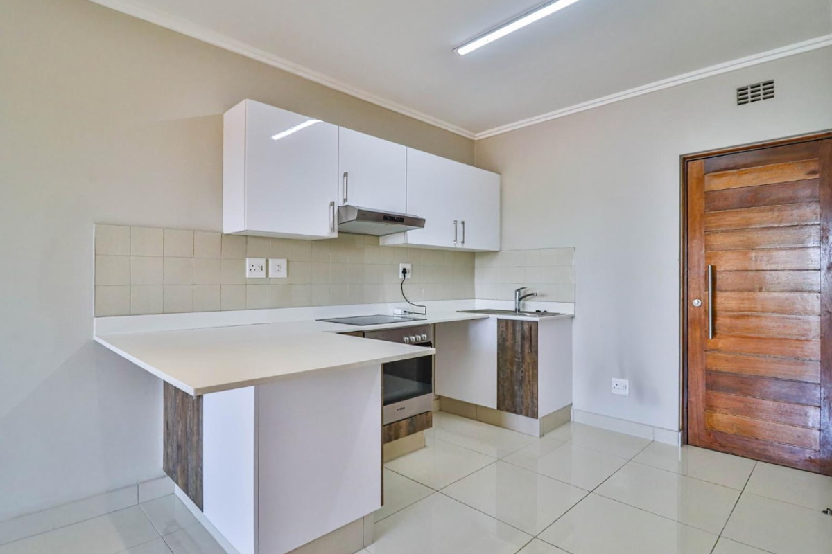 A clean, modern kitchen featuring white cabinetry, built-in oven and hob, tiled backsplash, and polished floor tiles, offering a functional and bright workspace.