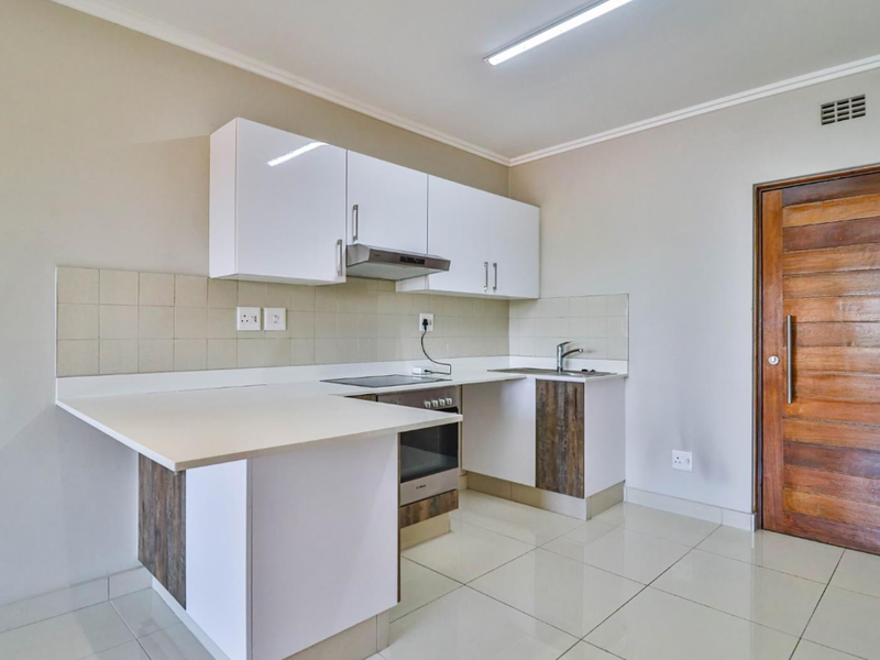 A clean, modern kitchen featuring white cabinetry, built-in oven and hob, tiled backsplash, and polished floor tiles, offering a functional and bright workspace.