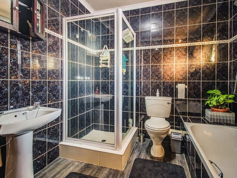 A functional bathroom featuring a pedestal sink, a separate shower enclosure, a toilet, and a bathtub, finished with dark marble-effect wall tiles.