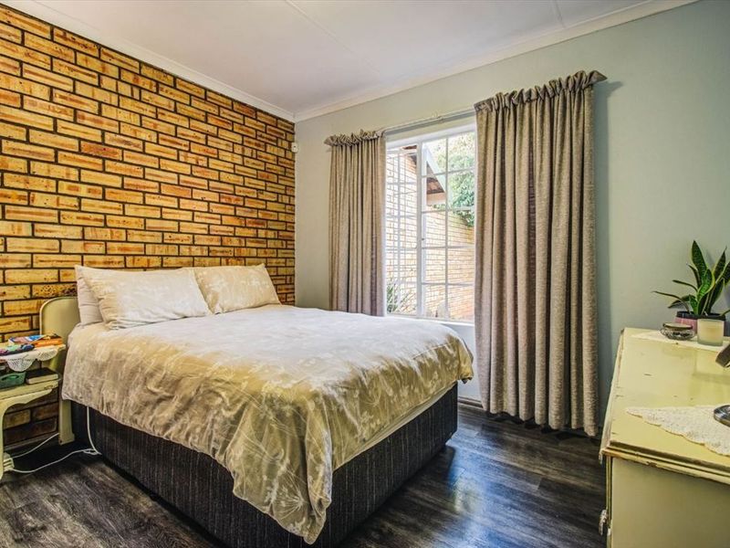 A bedroom featuring an exposed brick feature wall, laminate flooring, and a window with curtain tracks.
