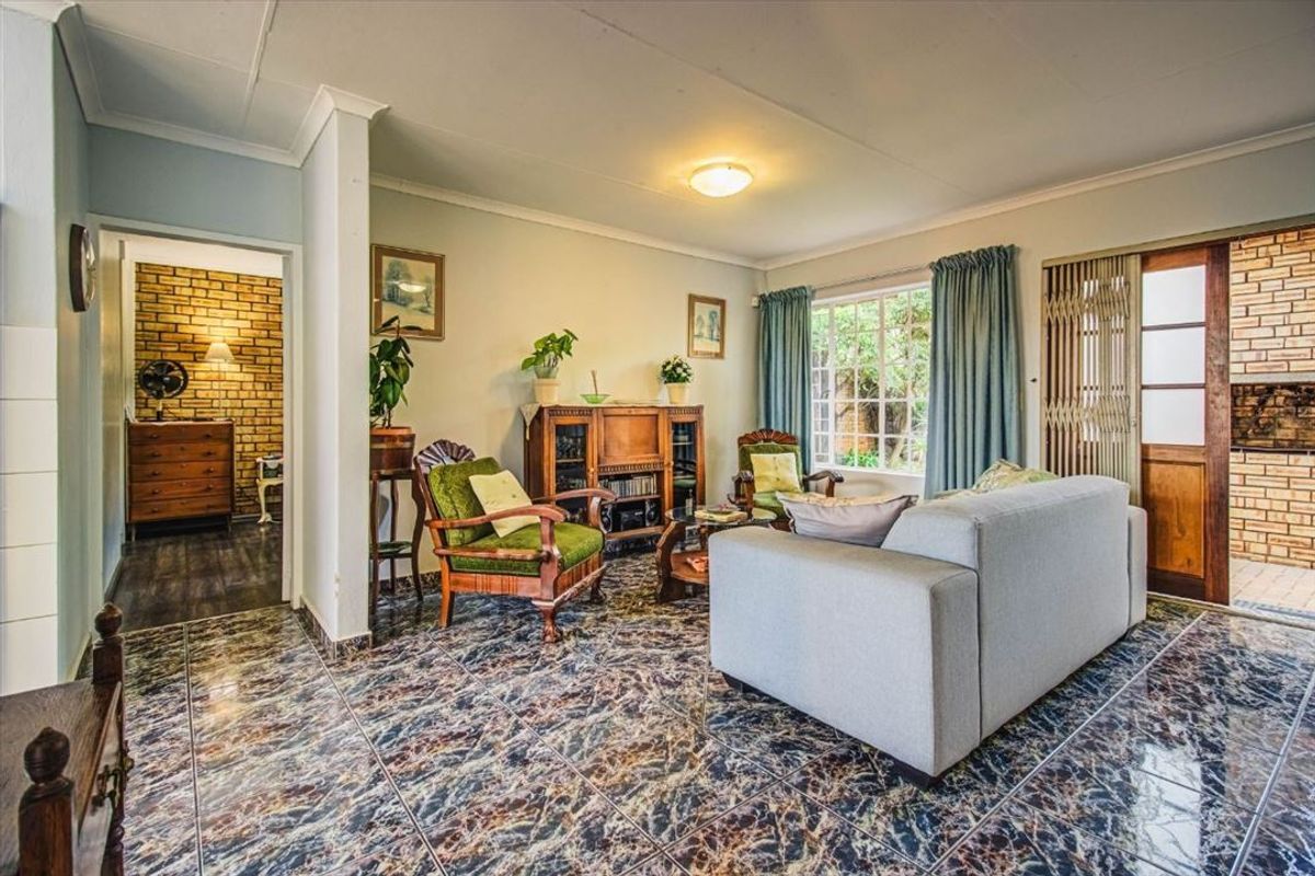 A living room featuring patterned tiled flooring, an exposed brick feature wall, and a sliding security gate leading to an outdoor area.