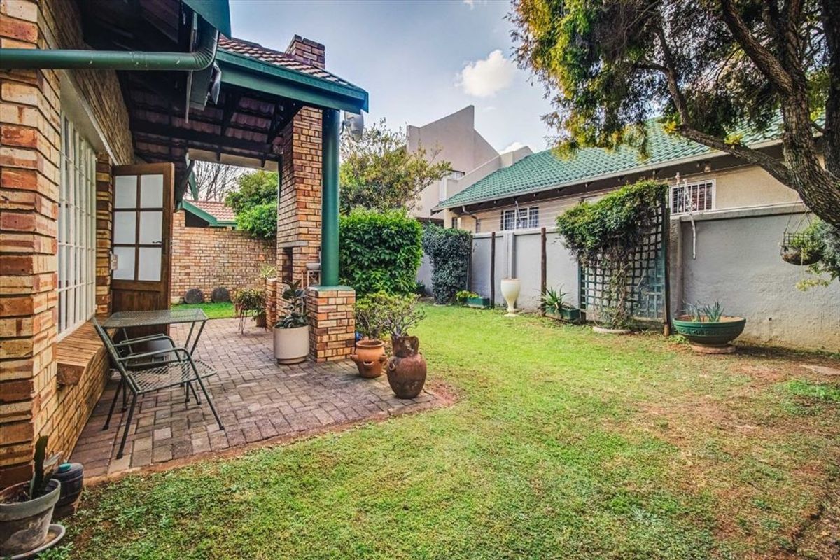 A private rear garden featuring a covered brick-paved patio with a built-in braai, established lawn, and perimeter walling.