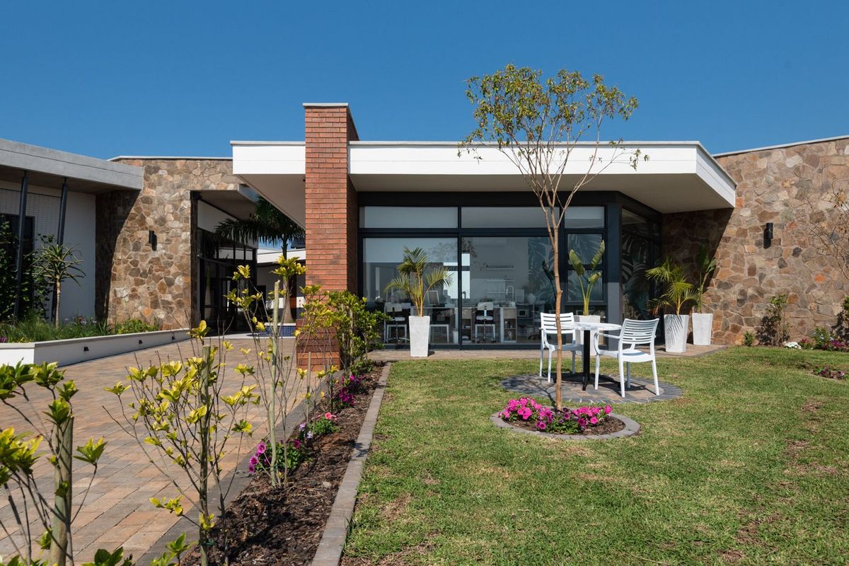 A well-maintained rear exterior featuring stone cladding, a brick chimney, large sliding glass doors, and a landscaped garden with a paved patio area.