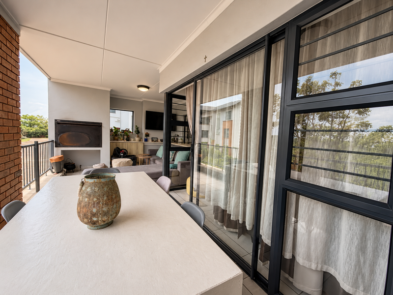 A covered balcony featuring a built-in braai, tiled flooring, and large sliding glass doors that provide seamless access to the interior living space.