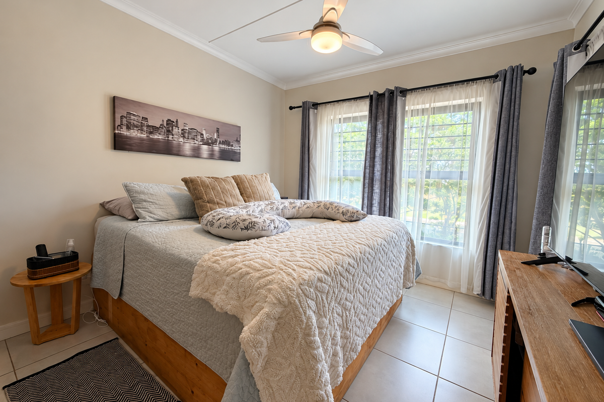 A well-maintained bedroom featuring tiled flooring, a ceiling fan, and large windows with security bars, offering a bright and comfortable living space.