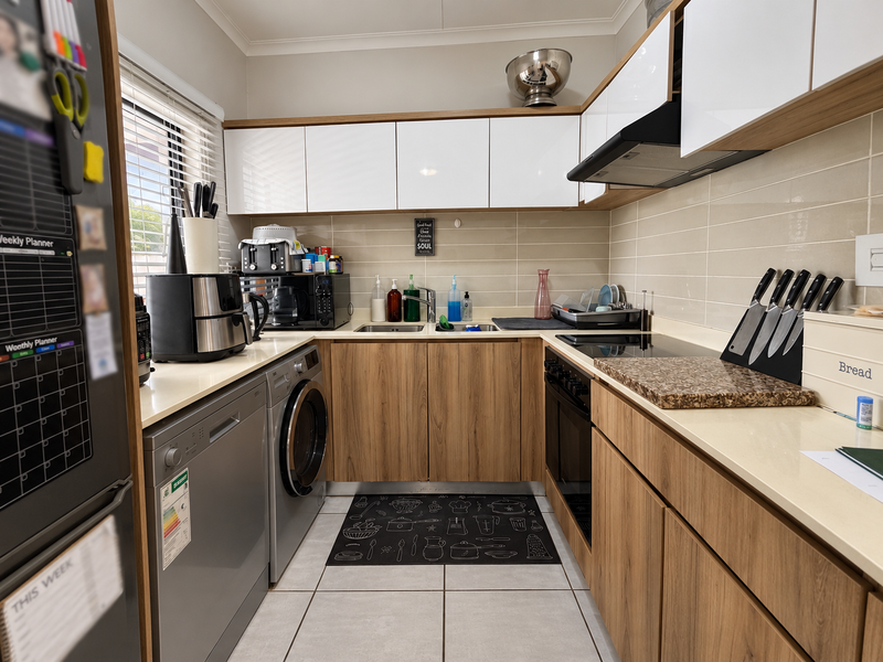 A modern, well-maintained kitchen featuring wood-grain lower cabinets, white upper cabinets, stone countertops, and integrated appliances including an oven and cooktop.